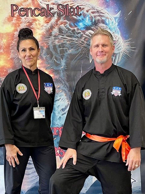 A man and a woman are posing in front of a banner that says pencak silat