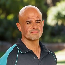 A man wearing a black and blue shirt looks at the camera