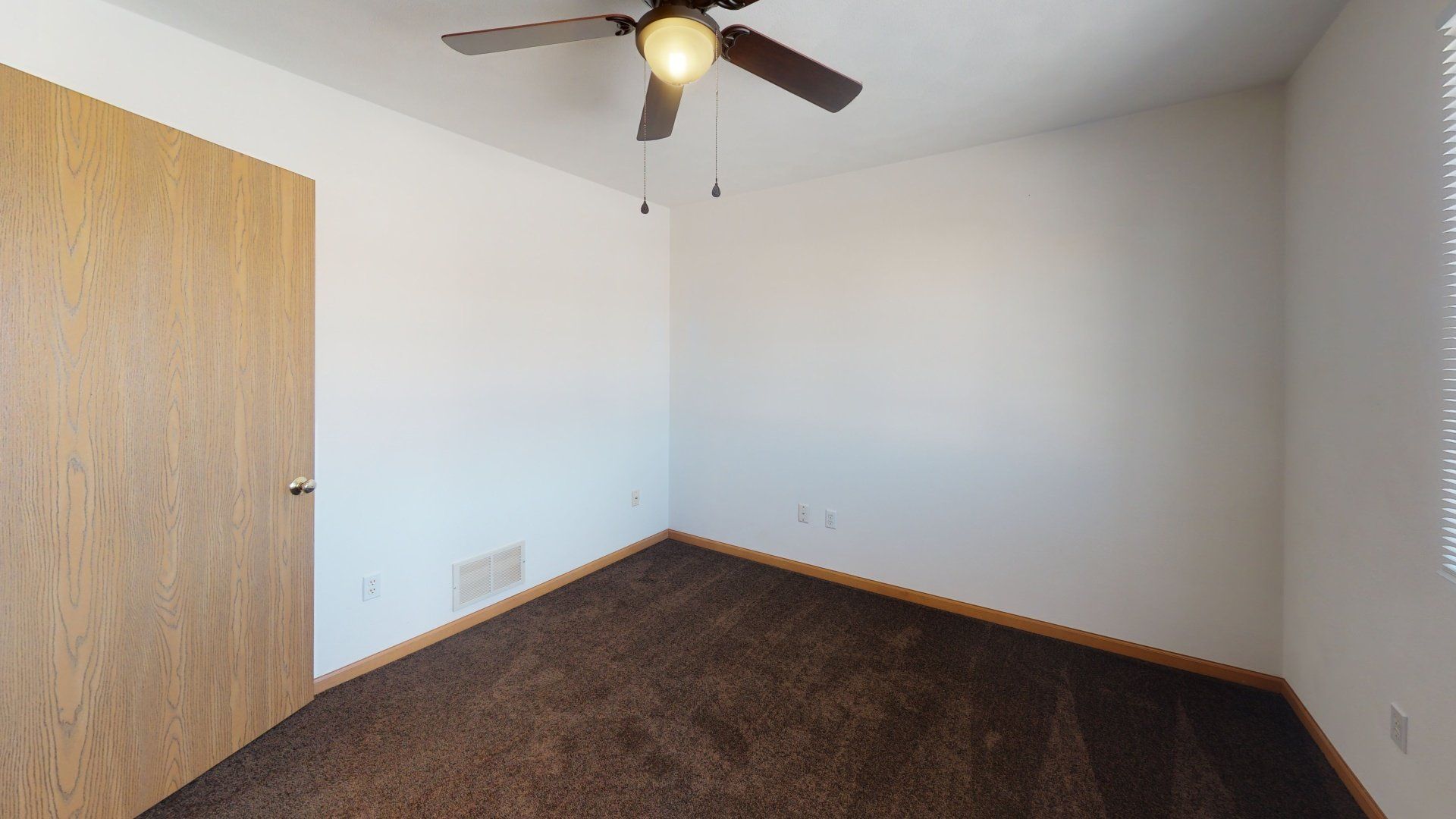 An empty bedroom with a ceiling fan and a door.