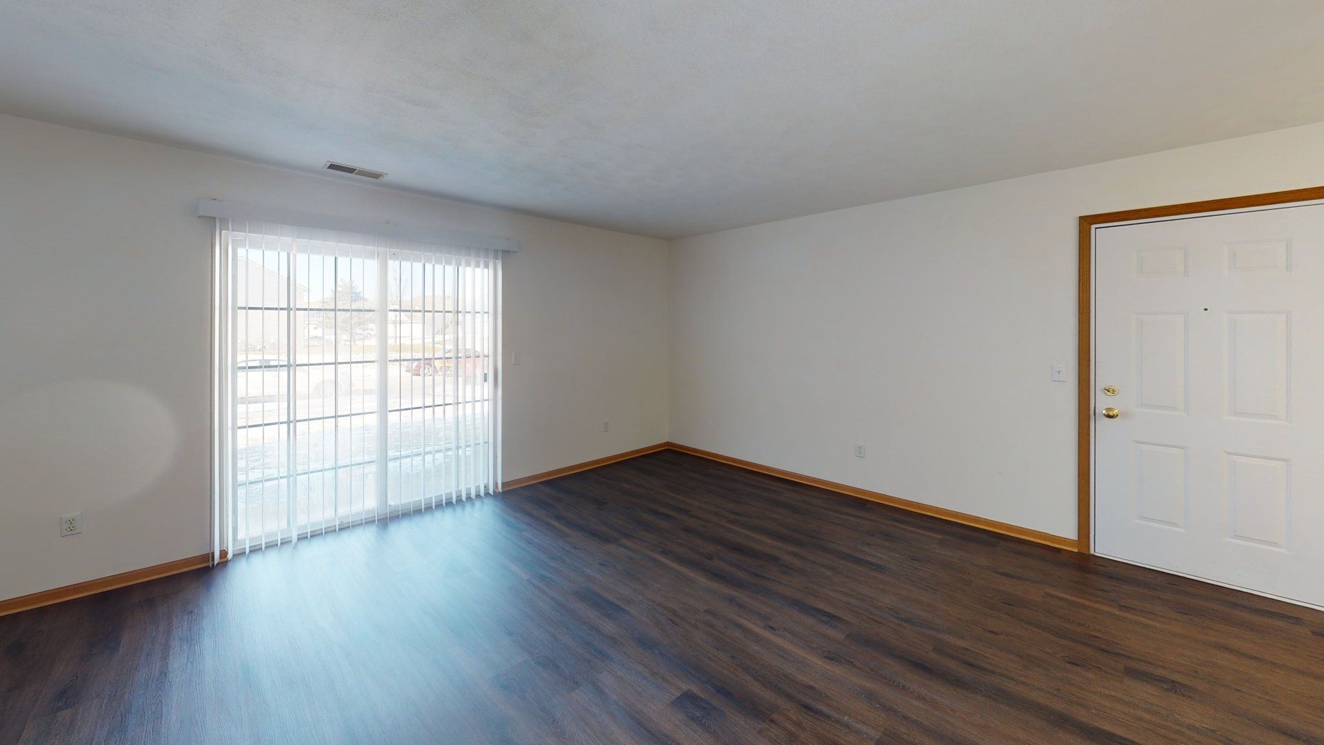 An empty living room with hardwood floors and sliding glass doors.