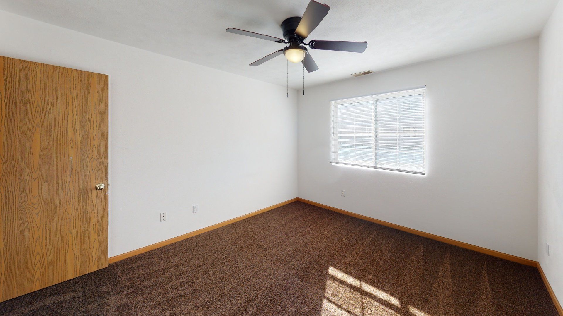 An empty bedroom with a ceiling fan and a window.