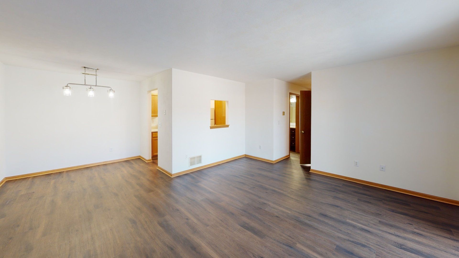 An empty living room with hardwood floors and white walls.