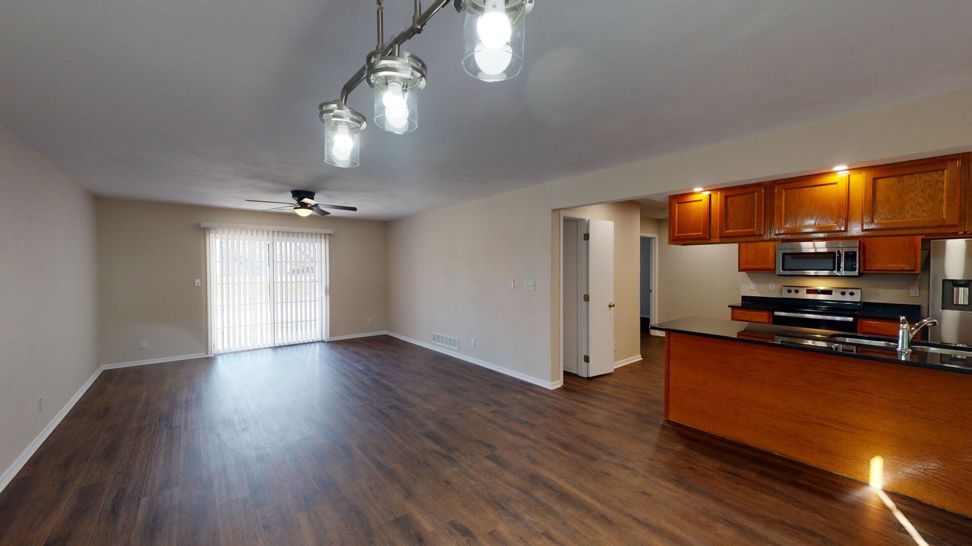 A living room with hardwood floors and a kitchen with stainless steel appliances.