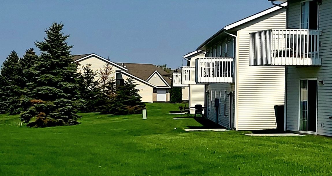 A row of apartment buildings with balconies and a lush green lawn in front of them.