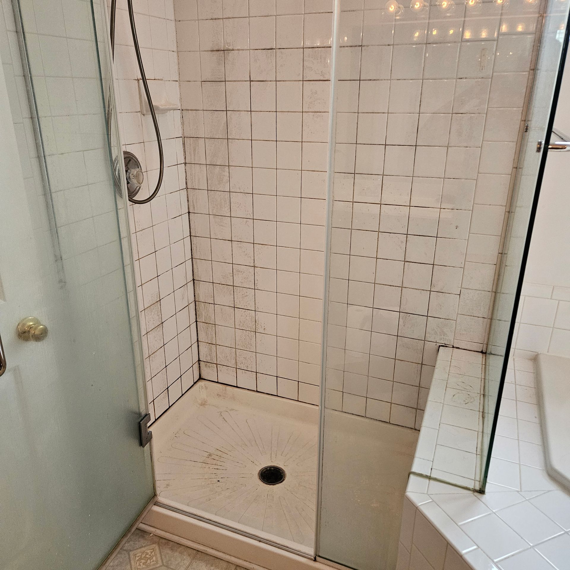 Small tiled shower stall with a showerhead, open door, and a drain in the floor.