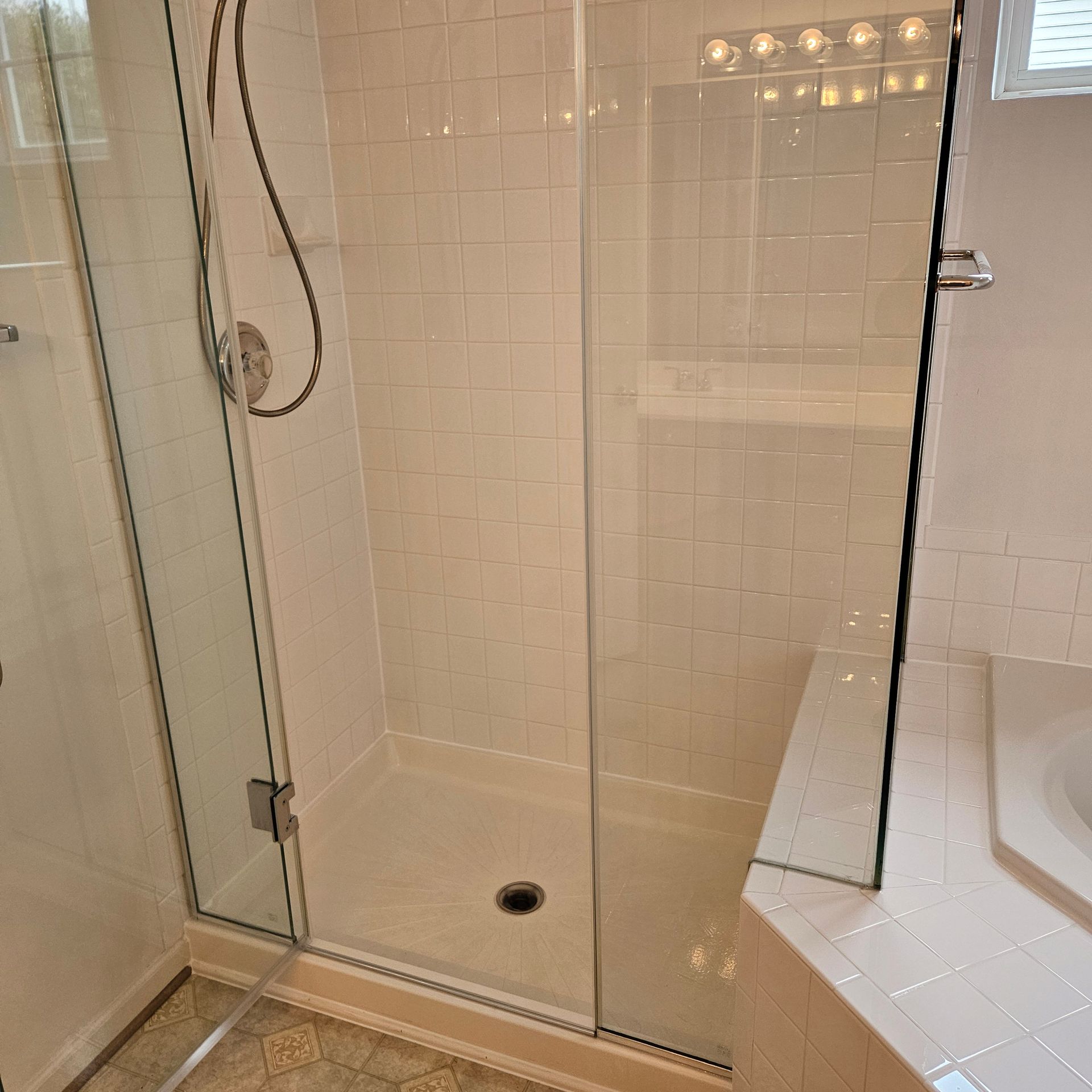Glass-enclosed tiled shower with built-in bench and chrome fixtures in a bathroom