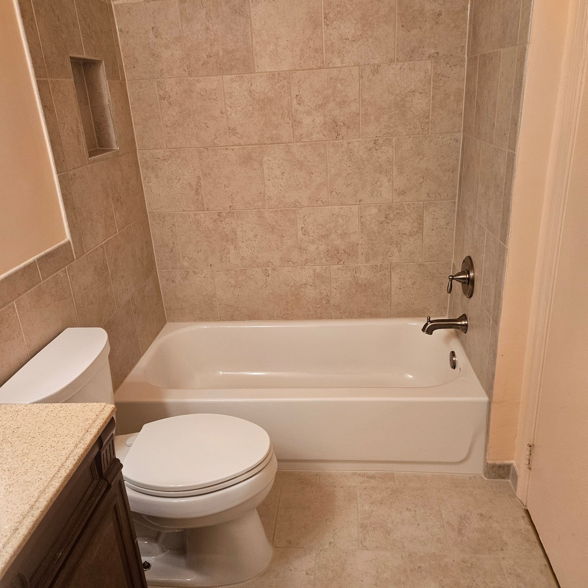 Small beige bathroom with a toilet, bathtub, and tan tile walls