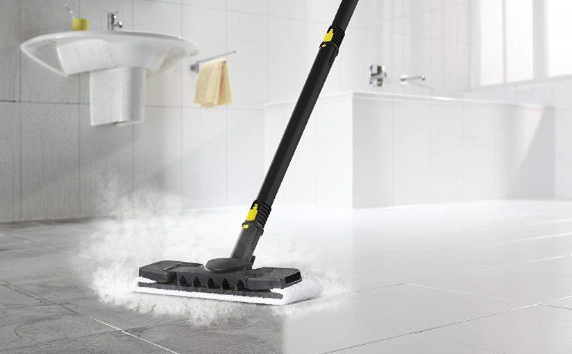 Steam mop cleaning a white tiled bathroom floor beside a sink and towel rack