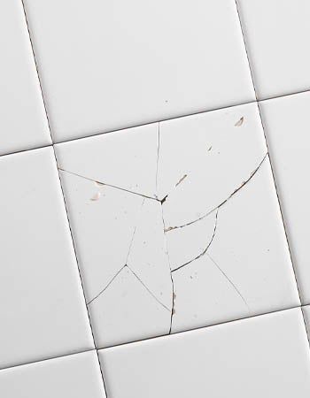 Cracked white tiled wall with a damaged central tile and visible fracture lines