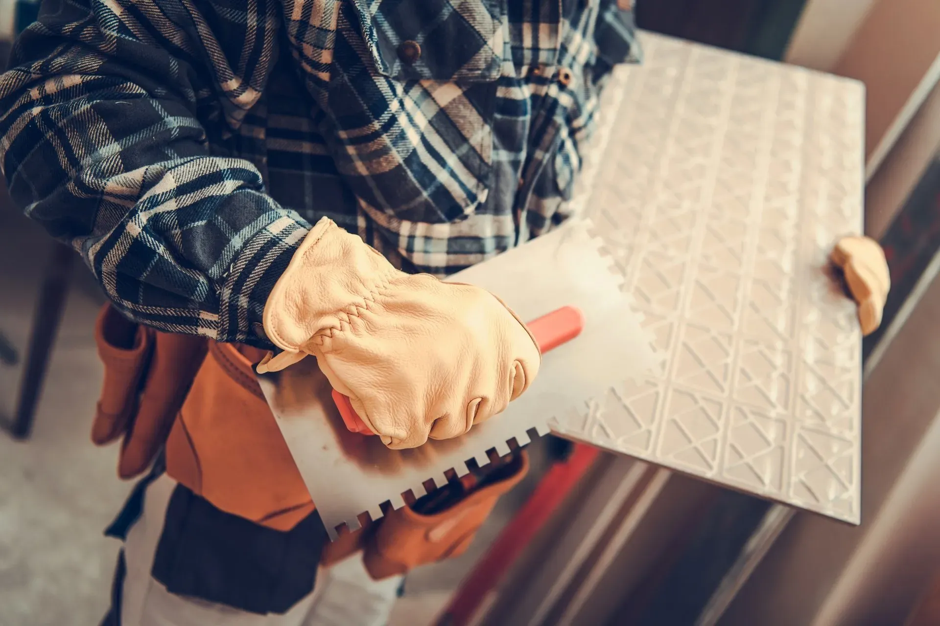 Person in plaid shirt holds a trowel and a textured tile or panel during home renovation.
