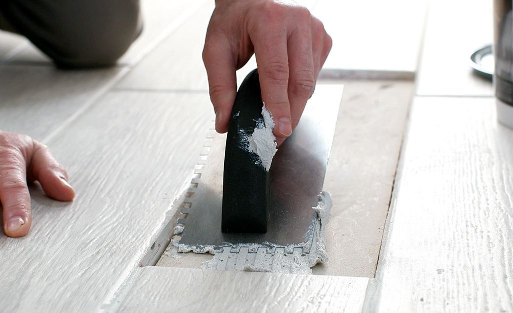 Hand using a trowel to spread gray mortar on a white surface