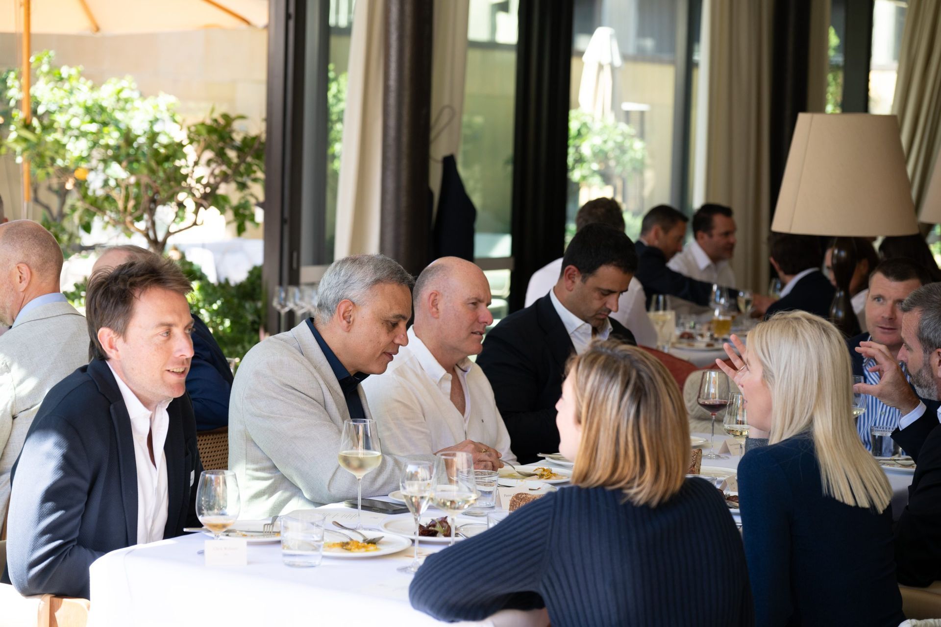 A group of people having a lunch meeting at a restaurant, seated around white-clothed tables.