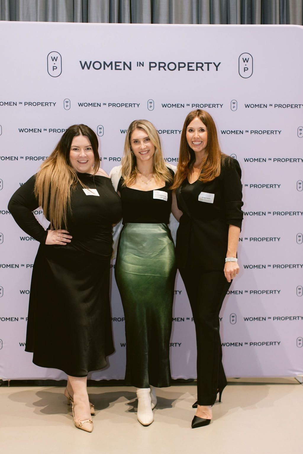 Three individuals pose smiling in front of a 