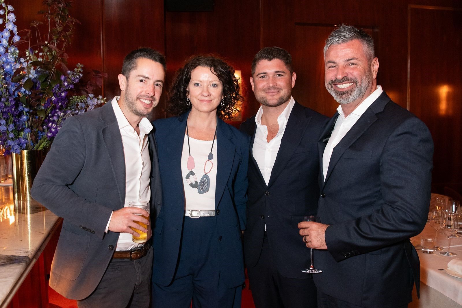 Four people smiling and posing in a dimly lit event space, wearing formal or business casual attire.