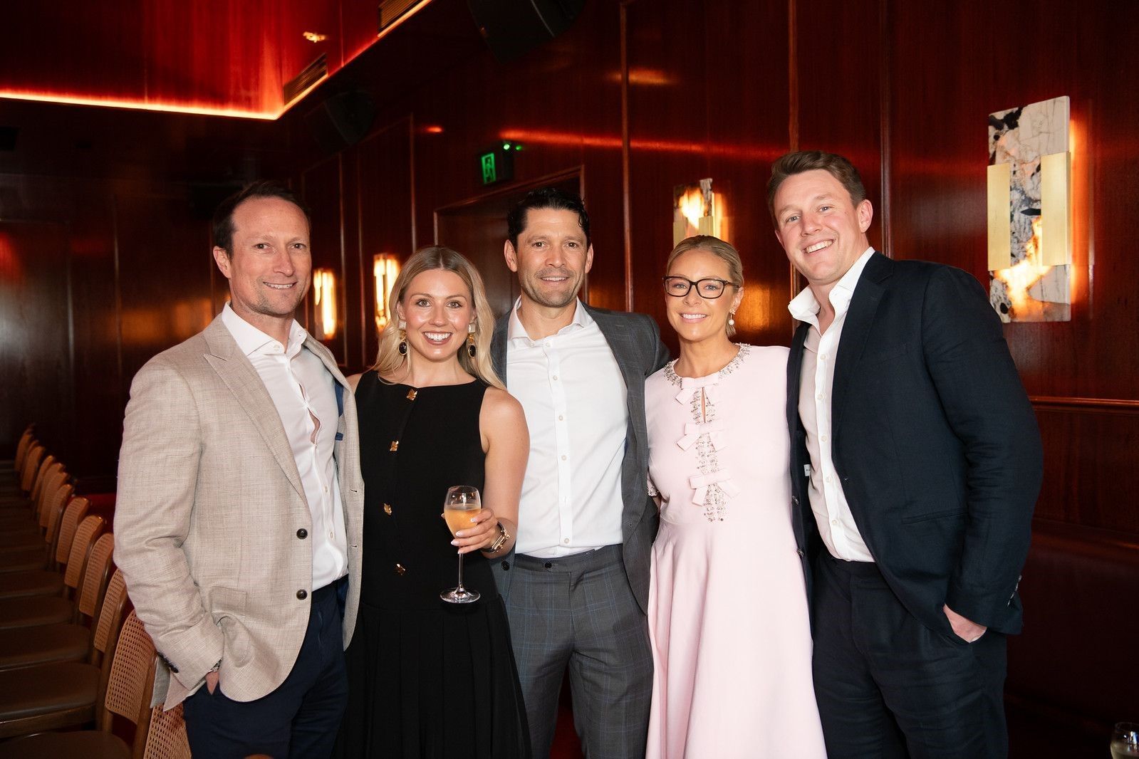 Five people stand smiling for a photo in a dimly lit, wood-paneled room.