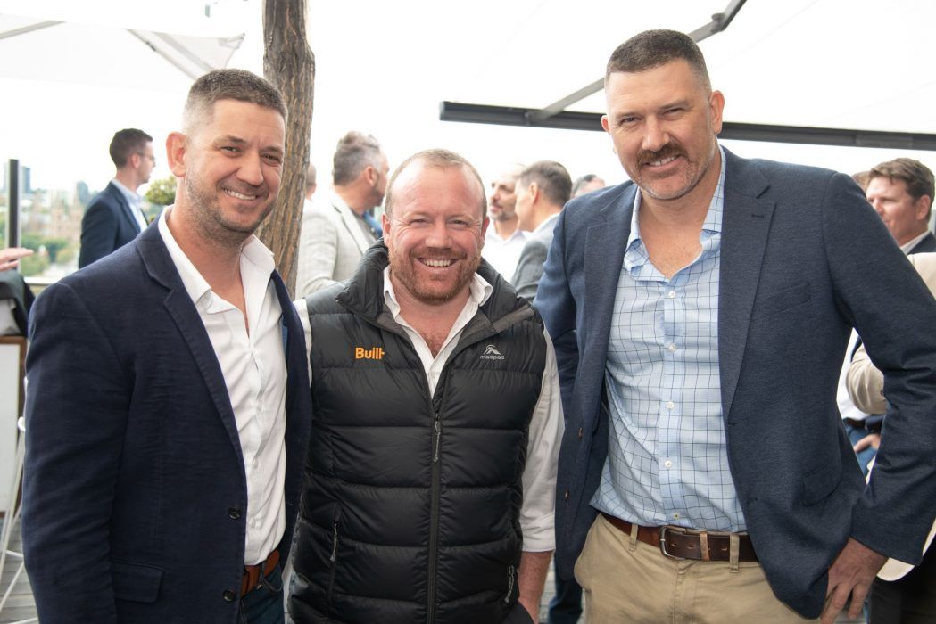 Three people smile while standing together outdoors at a daytime event.