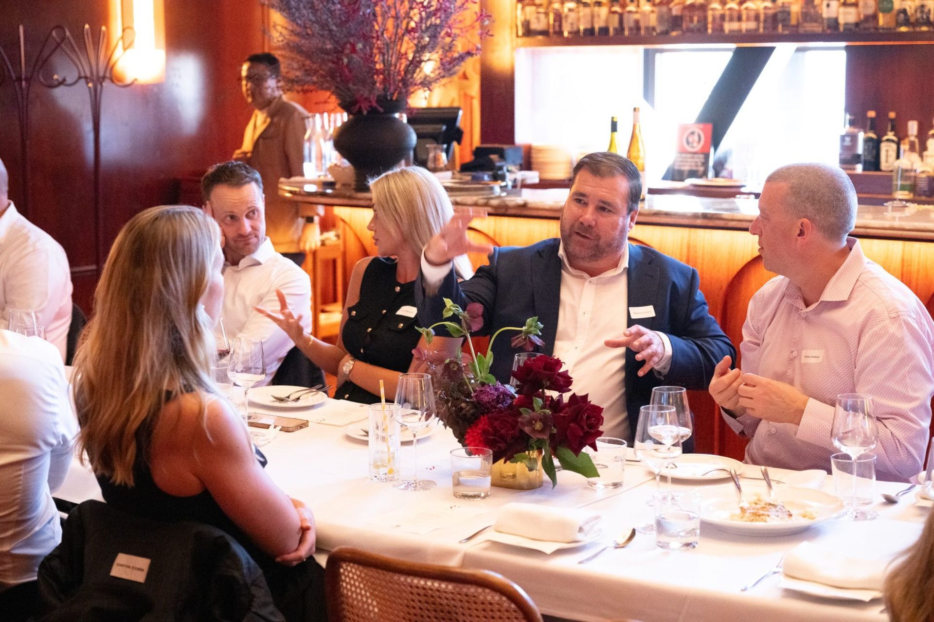 A group of people in business attire converse around a dining table at a restaurant.