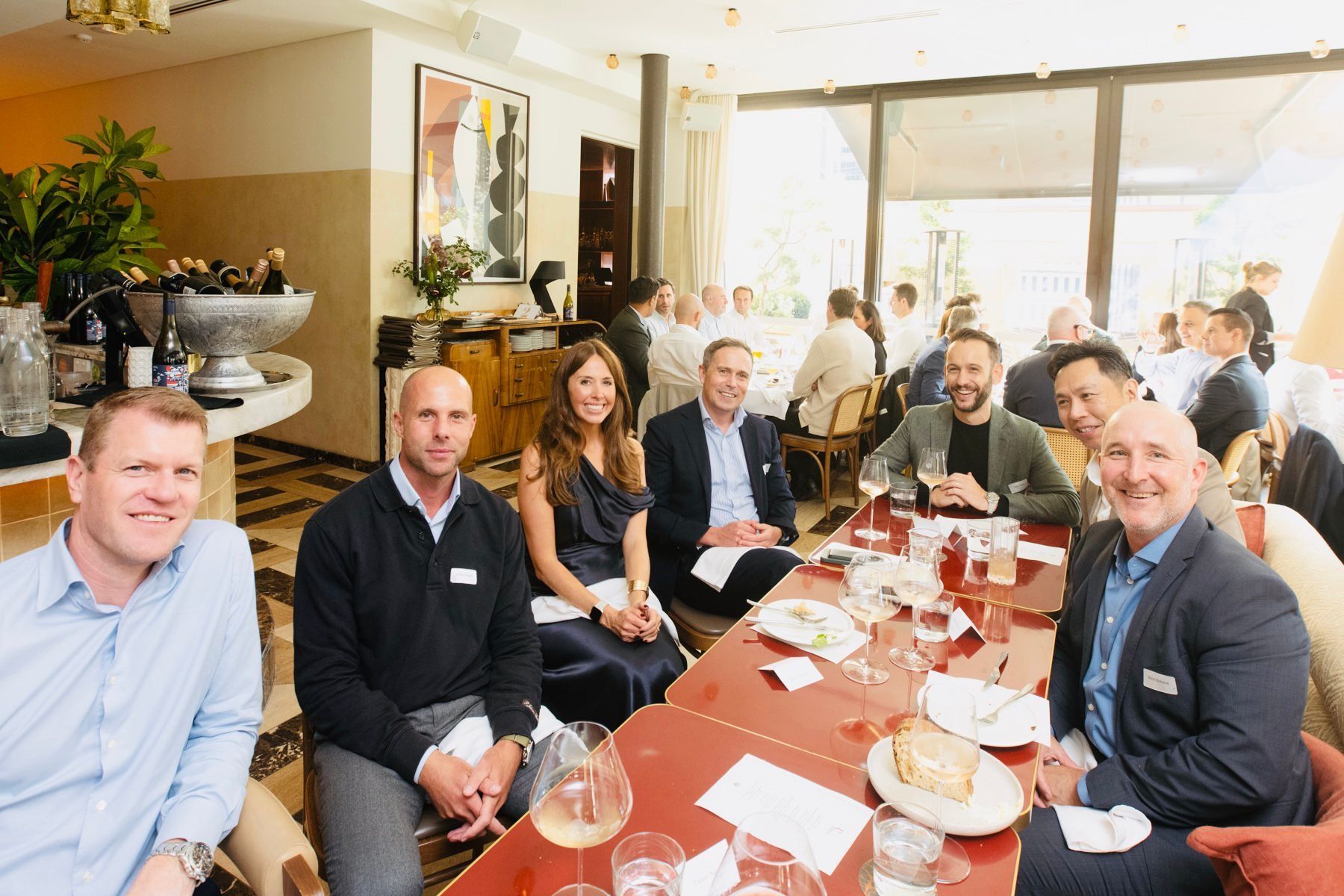 A group of people sits around a dining table at an indoor restaurant for a professional networking lunch.