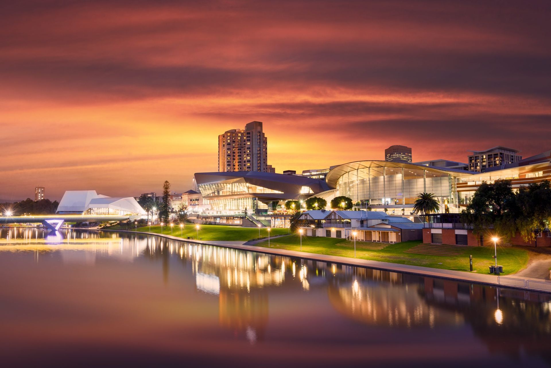 Modern architecture and city buildings along a calm river at sunset with warm orange and purple skies.