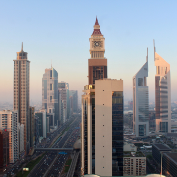 A view of the Dubai skyline along Sheikh Zayed Road, featuring tall skyscrapers and a prominent clock tower building.