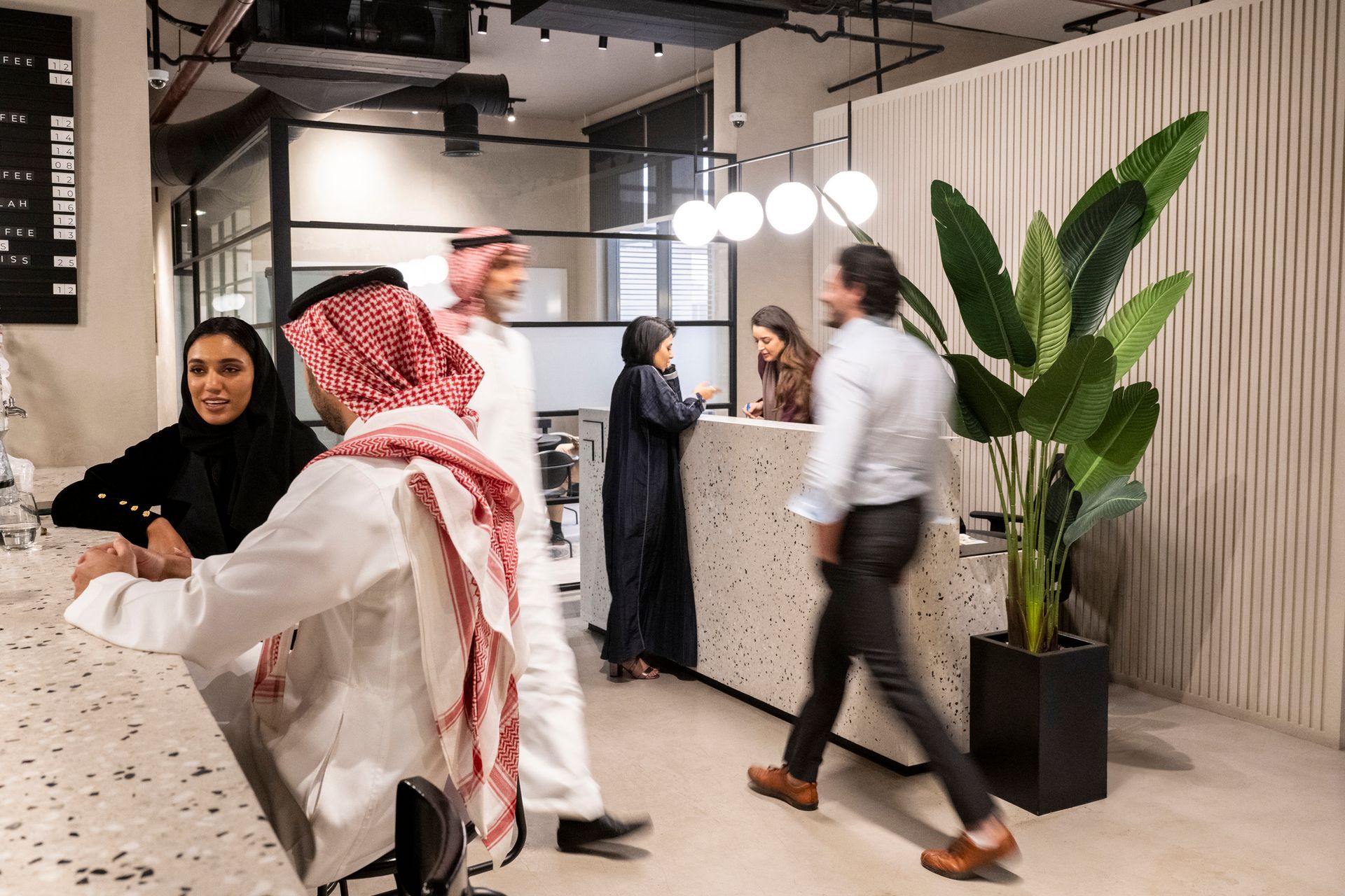 A diverse group of people in a modern, light-toned office lobby with a reception desk, green plant, and blurred motion.