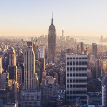 A high-angle view of the Manhattan skyline at sunset, featuring the Empire State Building as the central landmark.