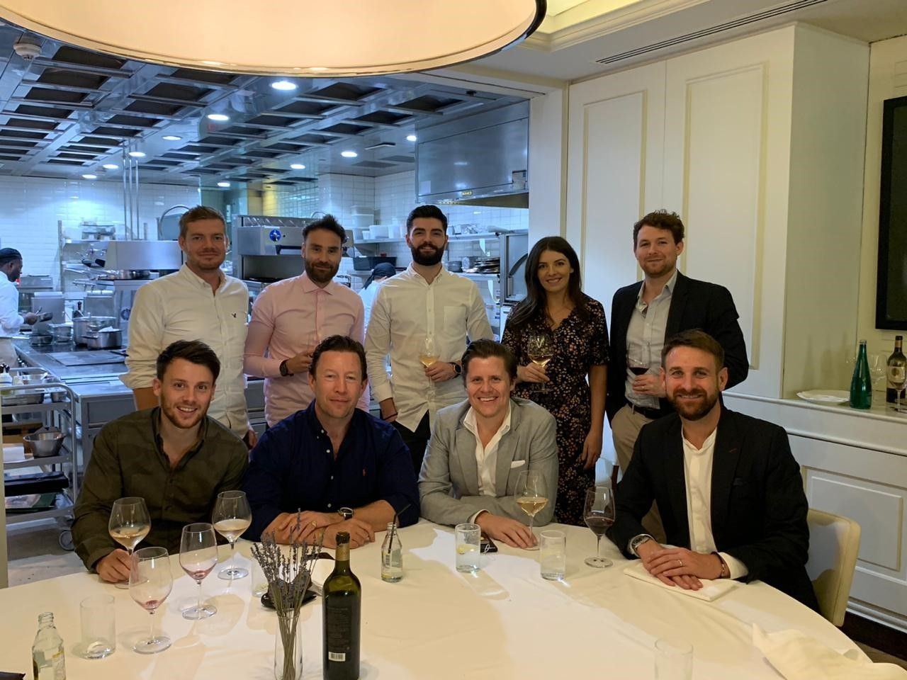 A group of ten people seated and standing around a dining table in a restaurant setting, smiling for a photo.