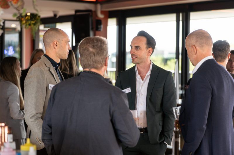 A group of professionals in business attire conversing and networking in a bright, indoor event space.