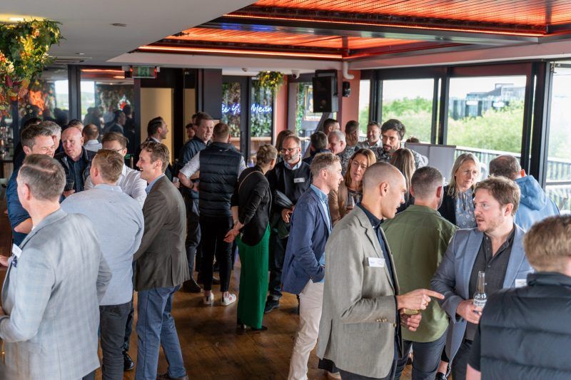 A diverse group of people networking and socializing in a well-lit, open-plan indoor event space with wooden floors.