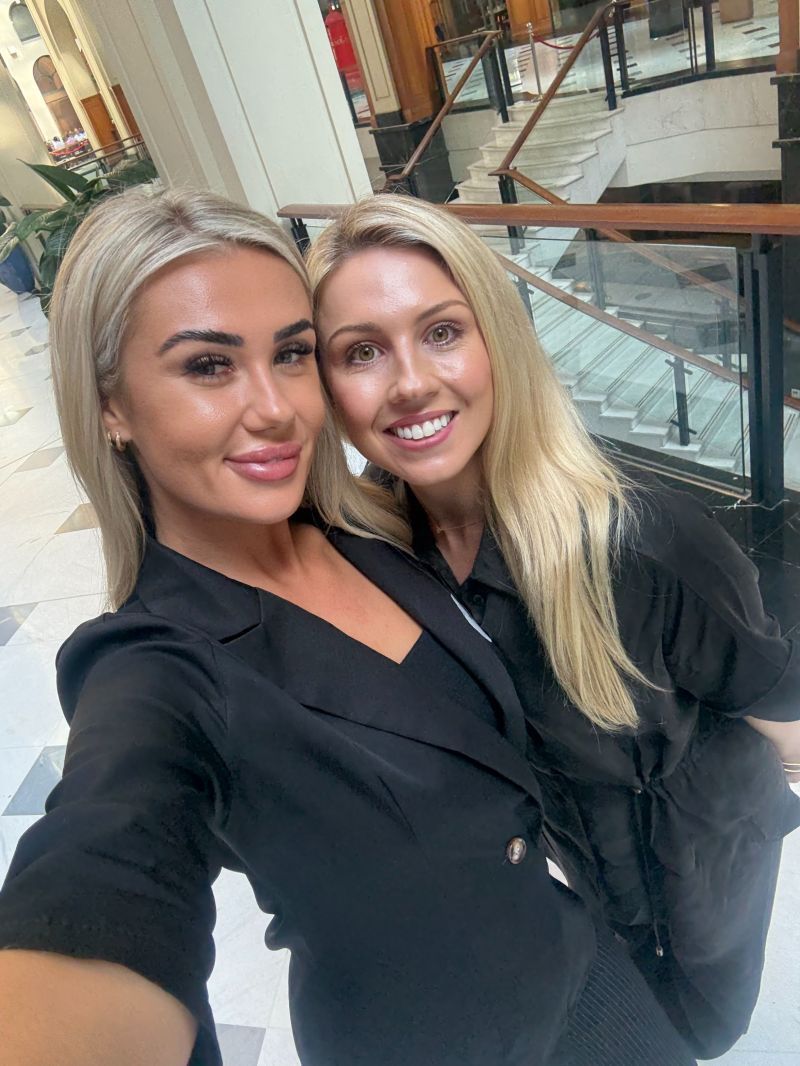 Two people with blonde hair smiling in a selfie while standing in a bright indoor shopping mall.