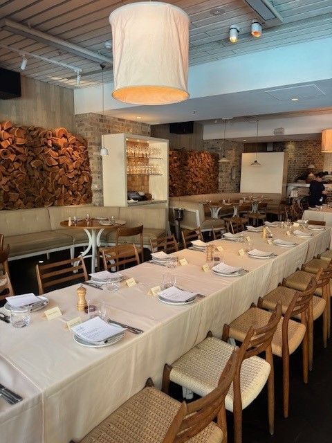 A long table set for a formal dining event in a restaurant with light wood walls decorated with stacked firewood.