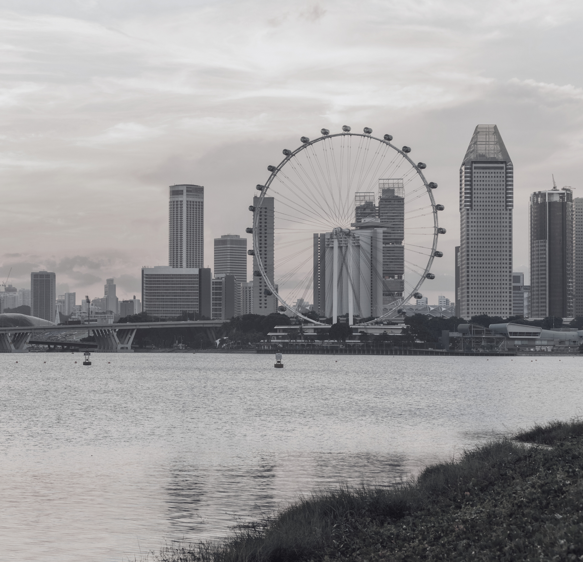 Black-and-white view of the Singapore Flyer giant observation wheel overlooking the harbor with surrounding skyscrapers.