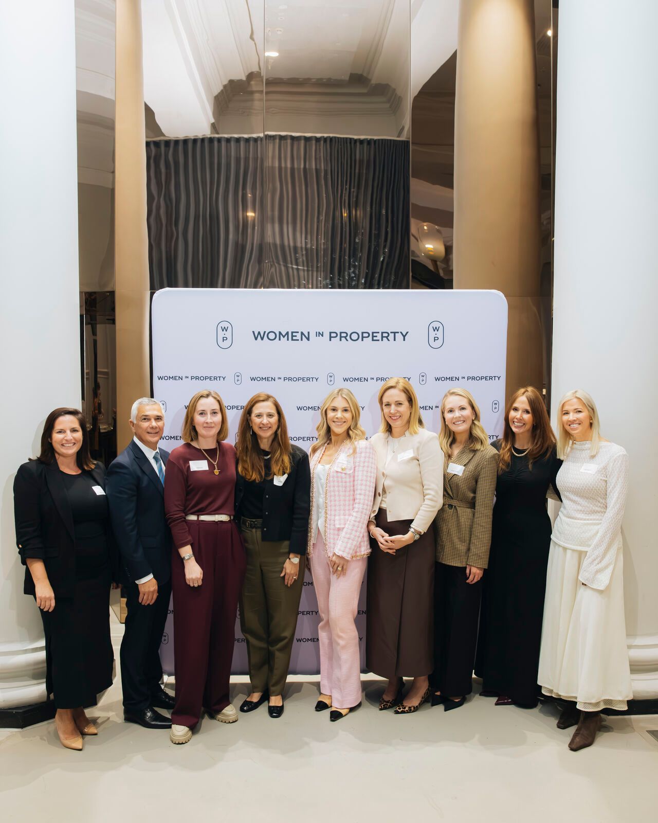 A group of nine people in professional attire stand smiling in a line before a