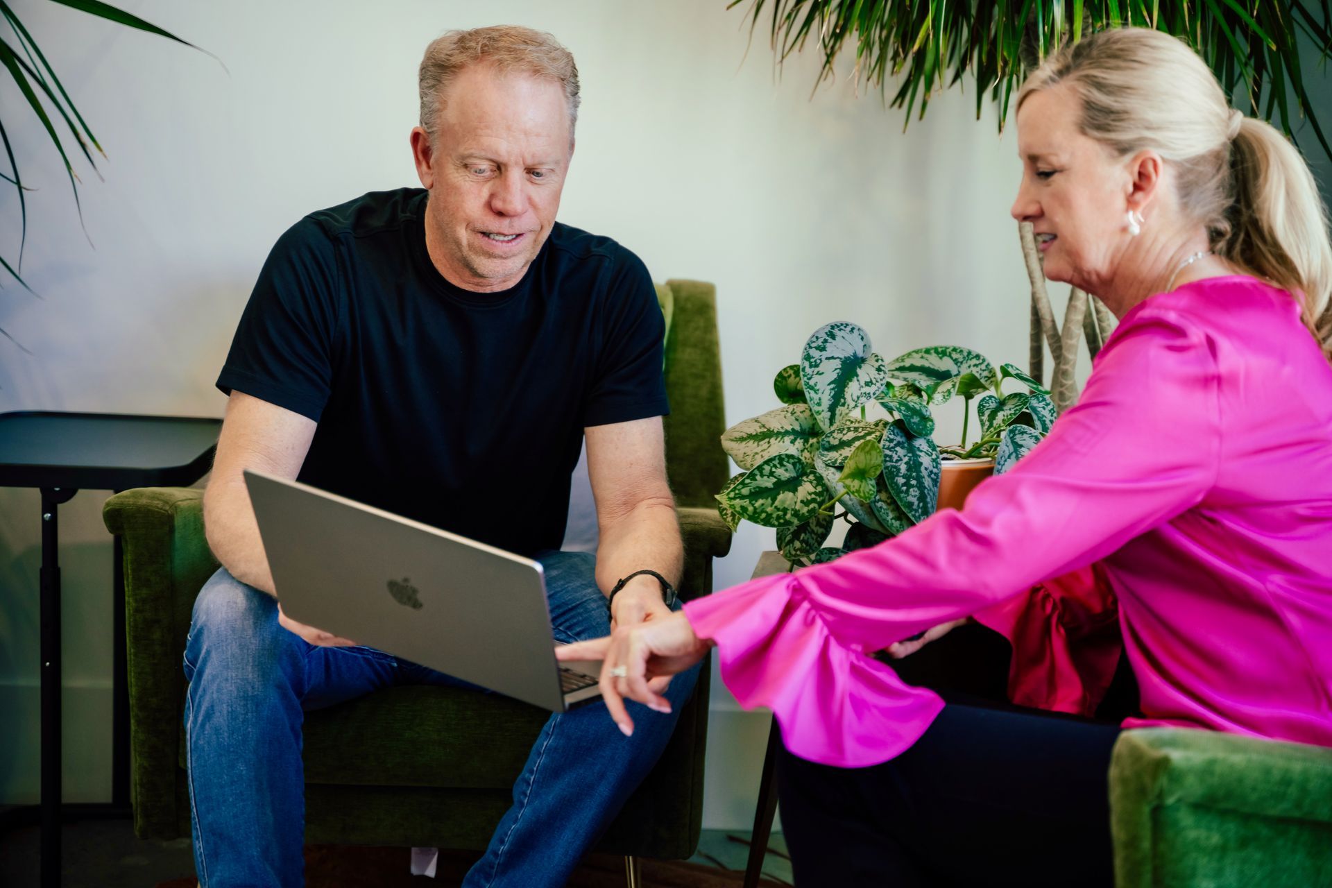 A man and a woman are sitting in chairs looking at a laptop computer.