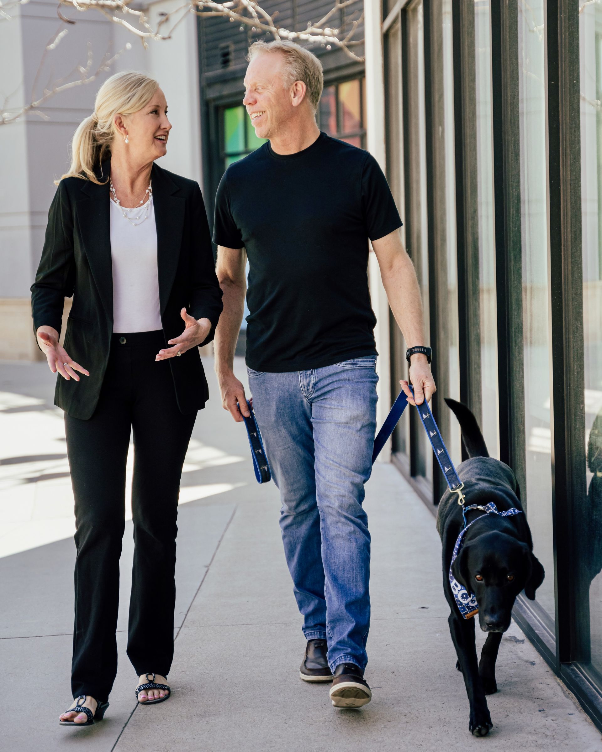 A man and a woman are walking a dog down a sidewalk.