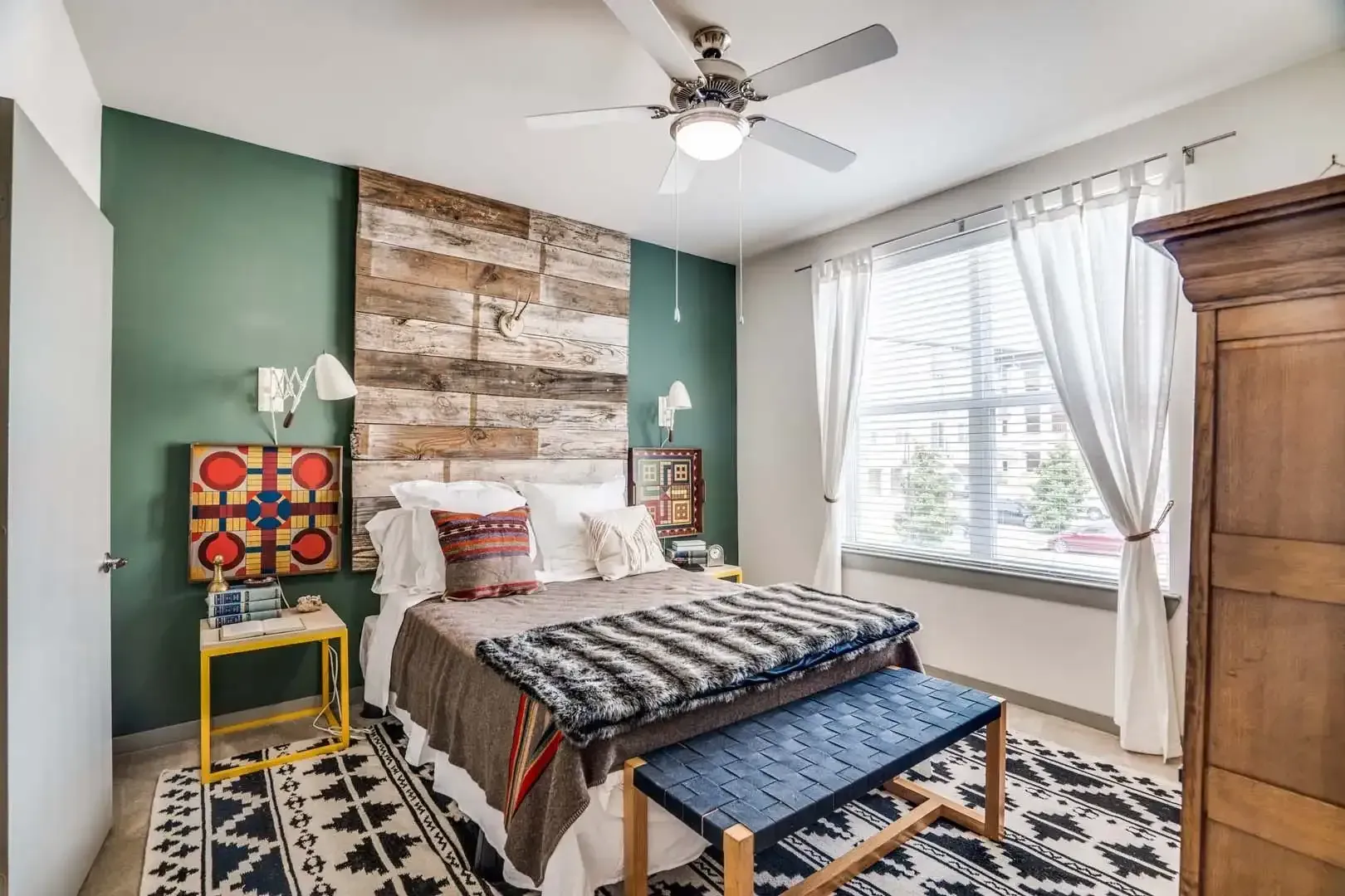 Bedroom with a rustic wood wall, bed with patterned blankets, and a blue bench at The Boat House, offers townhomes for rent in  Austin Ranch The Colony, TX.