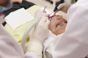 Patient in dental chair receiving dental work from two dentists.