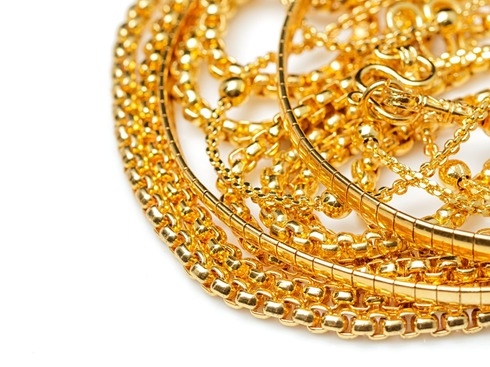 A close-up view of several layered gold necklaces with intricate chain designs and small, spherical beads.