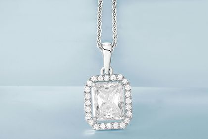 A radiant-cut diamond pendant necklace with a halo setting on a silver chain against a pale blue background.