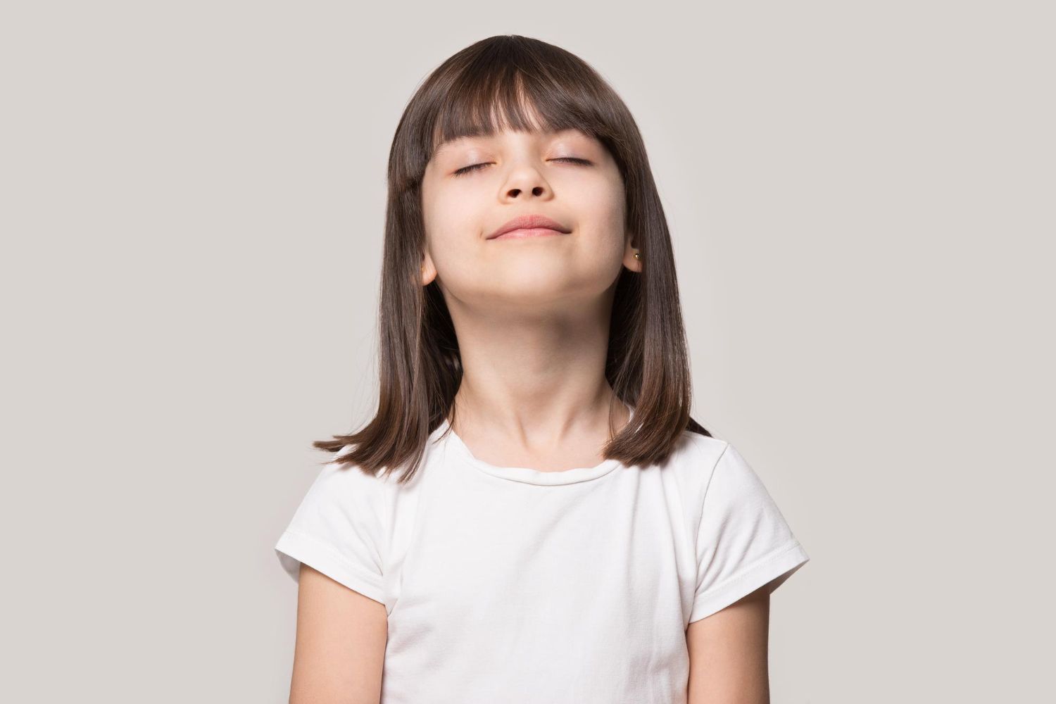 Girl with eyes closed, tilting her head slightly upward, wearing a white t-shirt.