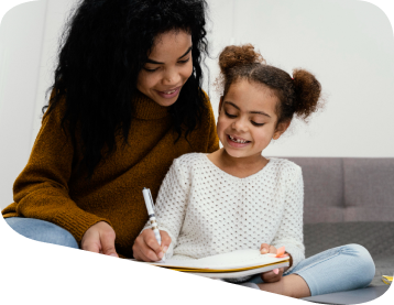 Woman helps child write in a notebook; both smiling.