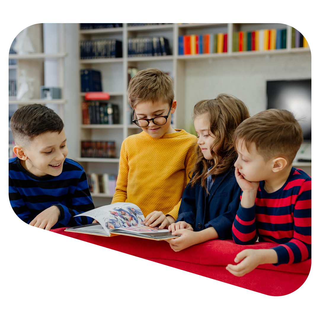 Four children gathered around a book, smiling and looking at the pages in a library.