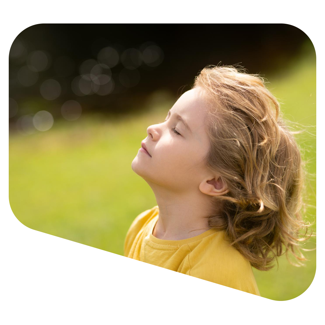 Child with eyes closed, tilted head up, enjoying sunlight outdoors.