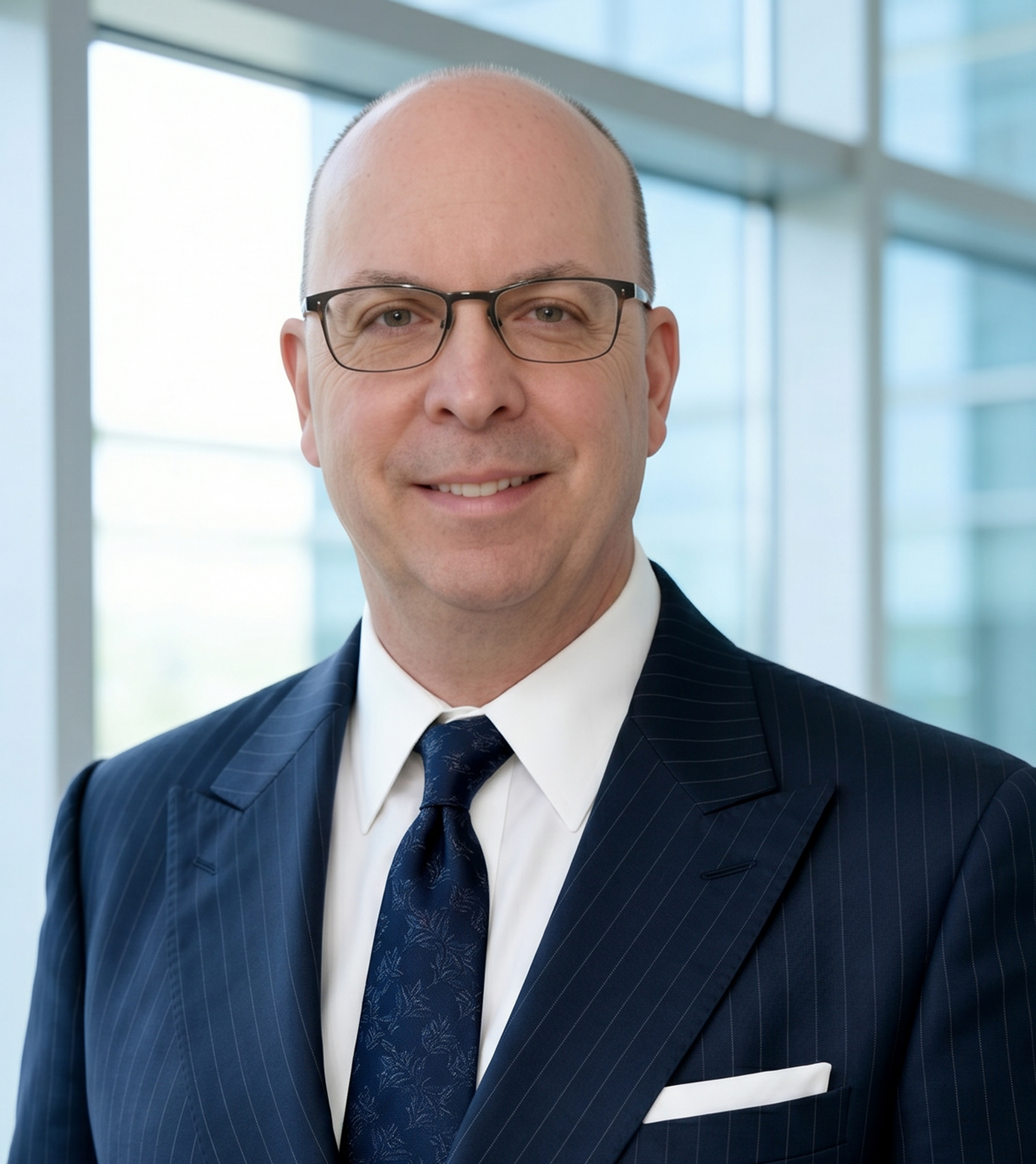 Business professional in a navy suit and glasses standing in a bright office with large windows