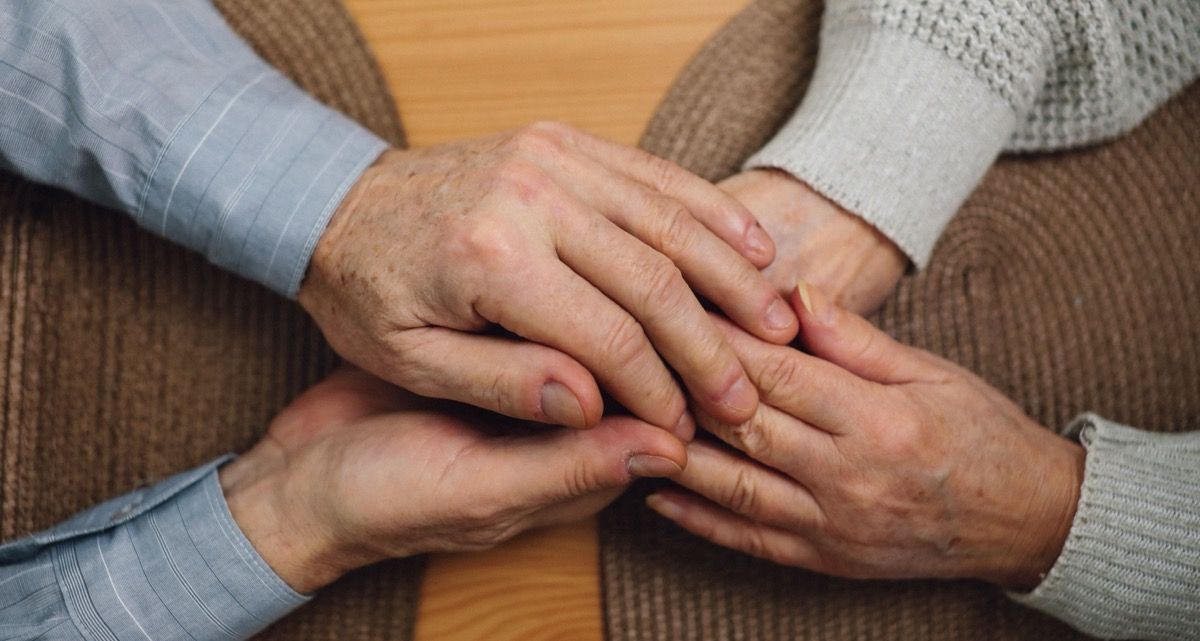 Three pairs of hands gently stacked together in a circle of support on a brown sweater.