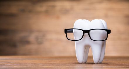 White tooth wearing black glasses on a wooden surface, against a blurred wooden background.