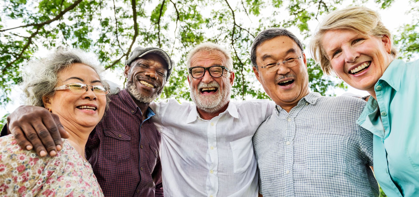 Smiling group of five people outdoors in a bright, leafy setting