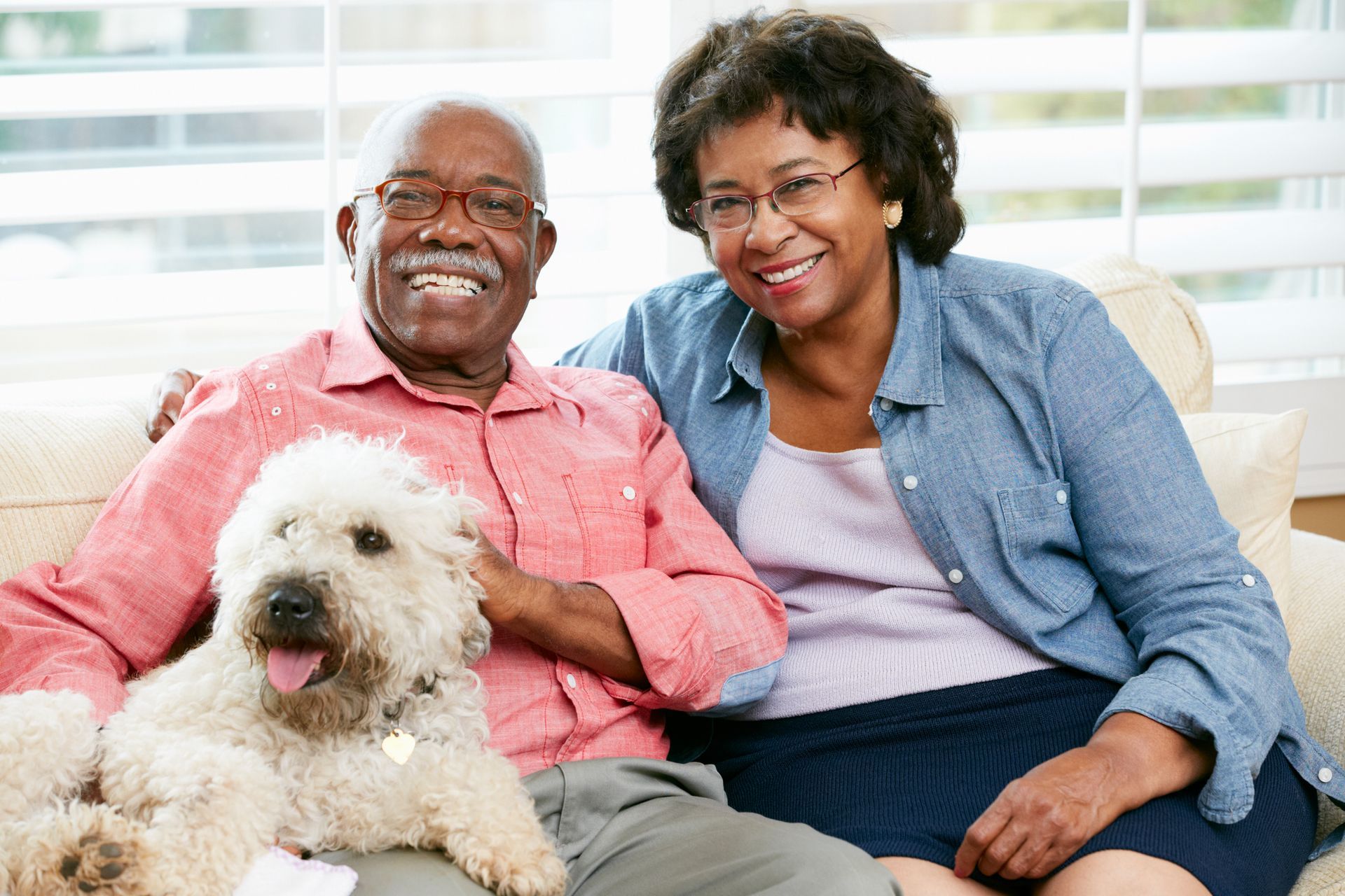Smiling couple on a couch with a fluffy white dog in a bright living room