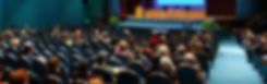 A blurry picture of a crowd of people sitting in an auditorium.
