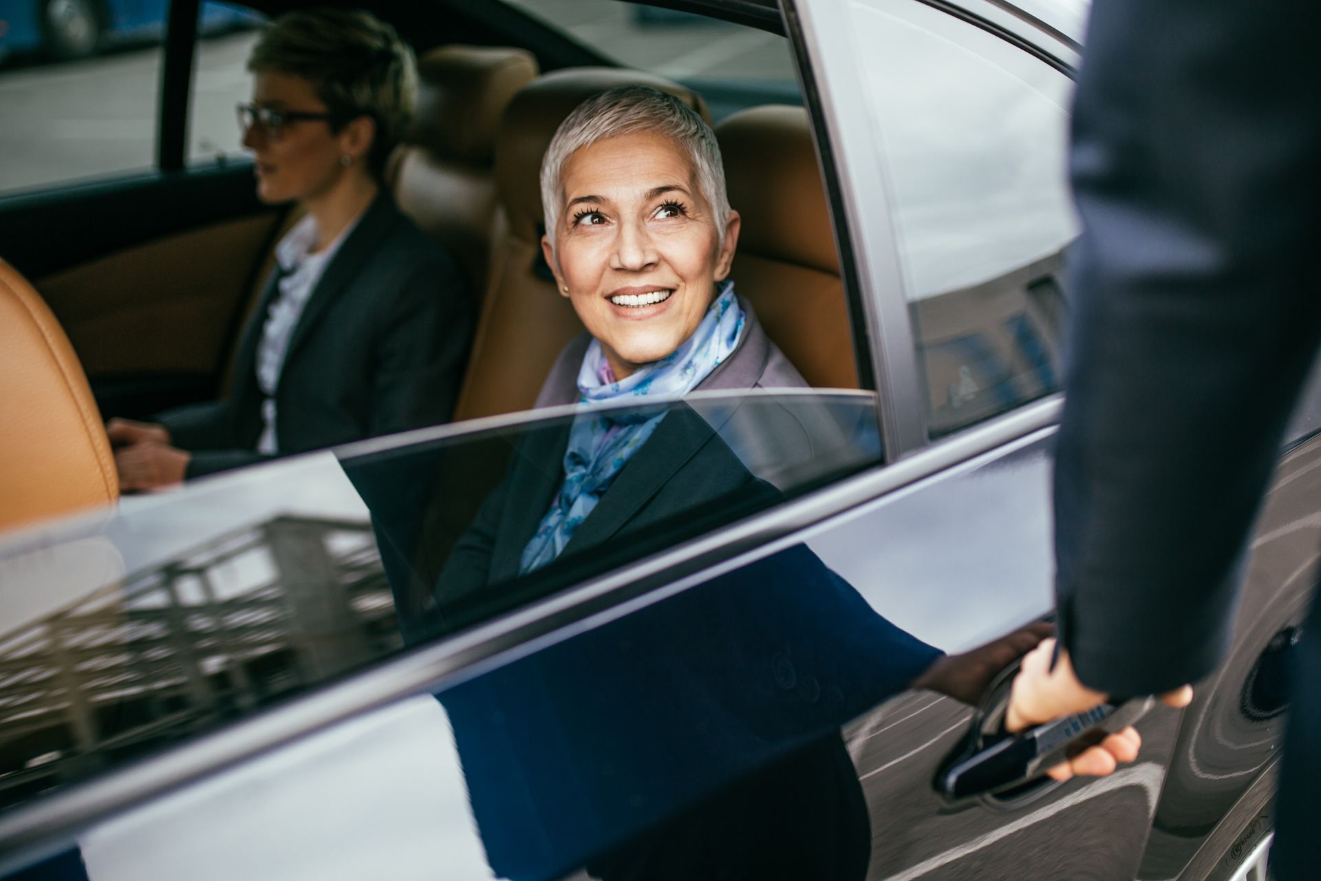 A woman is sitting in the back seat of a car while a man opens the door.